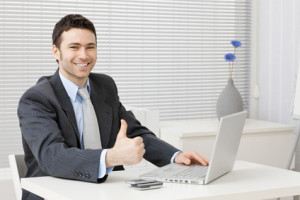 Happy young businessman showing success with thumb up at office, smiling.